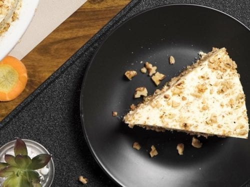 a slice of a two-layered carrot walnut cake with white frosting on a white plate