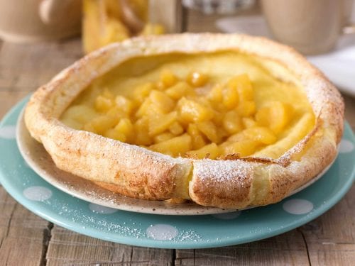 baked dutch baby pancake filled with fruit on a blue and white plate