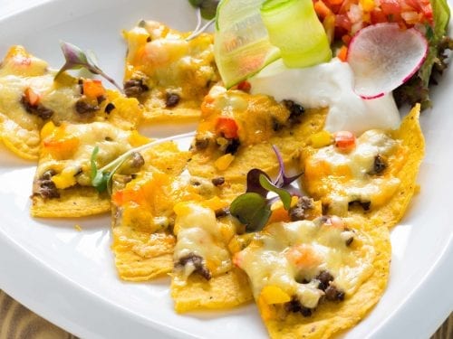 nacho chips on a white plate dipped in a cheesy meat sauce