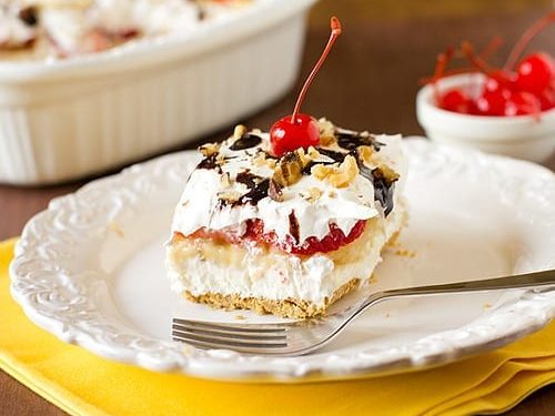 No-Bake Banana Split Cake Recipe, banana split cake with graham cracker crust, frosting, and cherries