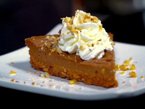 No Bake Nutella Cheesecake, Nutella cheesecake slice topped with chopped hazelnuts and whipped cream and served on a white plate