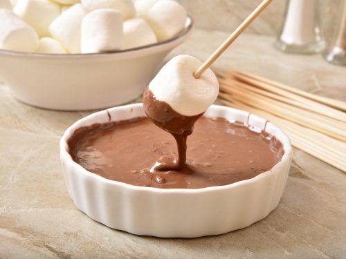 S'mores pops or marshmallow on a stick, dipped in a bowl of melted chocolate