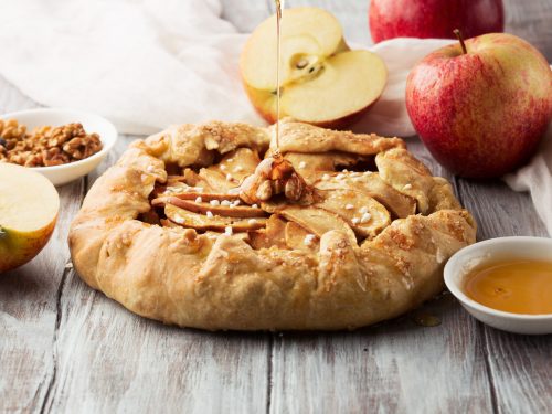 homemade crostata with ripe apples, nuts and maple syrup on rustic white wooden background, selective focus