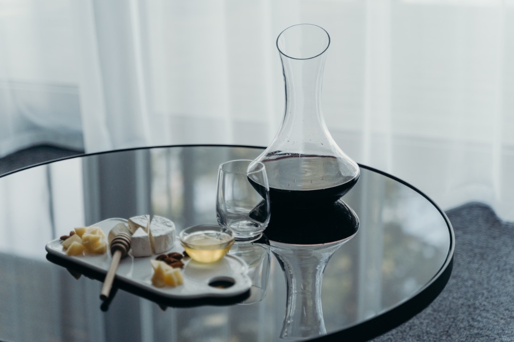 Red wine in a glass decanter, with a stemless wine glass and charcuterie on the side