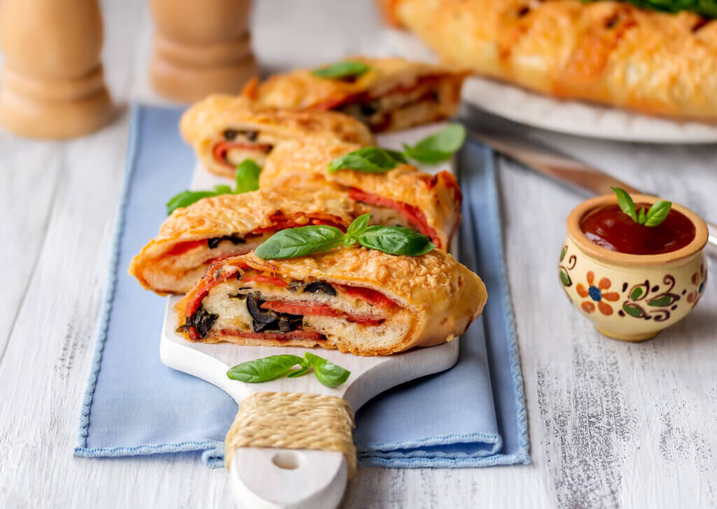 stromboli vs calzone, sliced italian stromboli stuffed with salami, cheese, black olive and tomato sauce on table