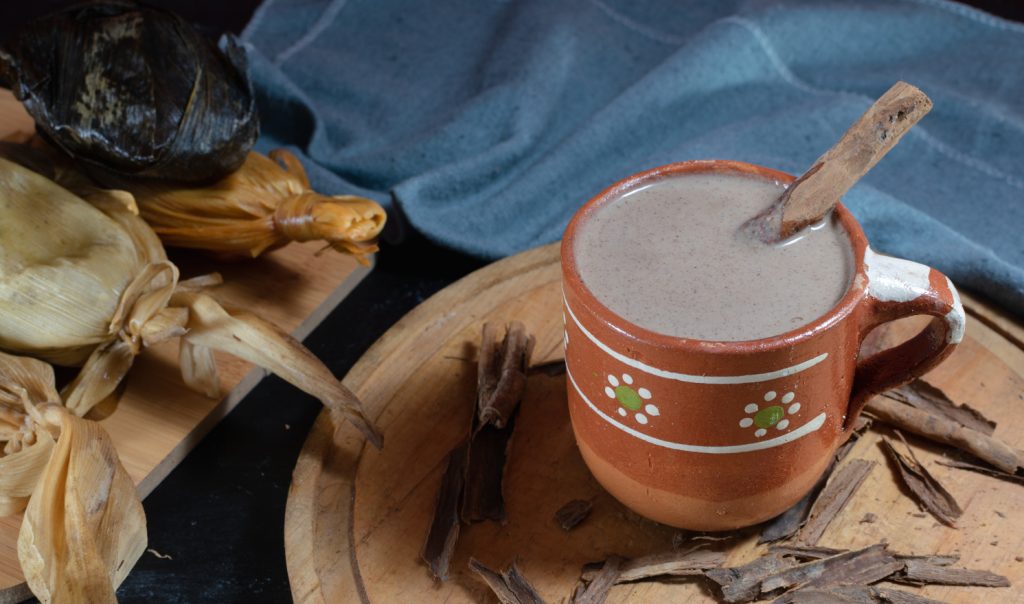 Taza artesanal con champurrado y tamales sobre una tabla de made