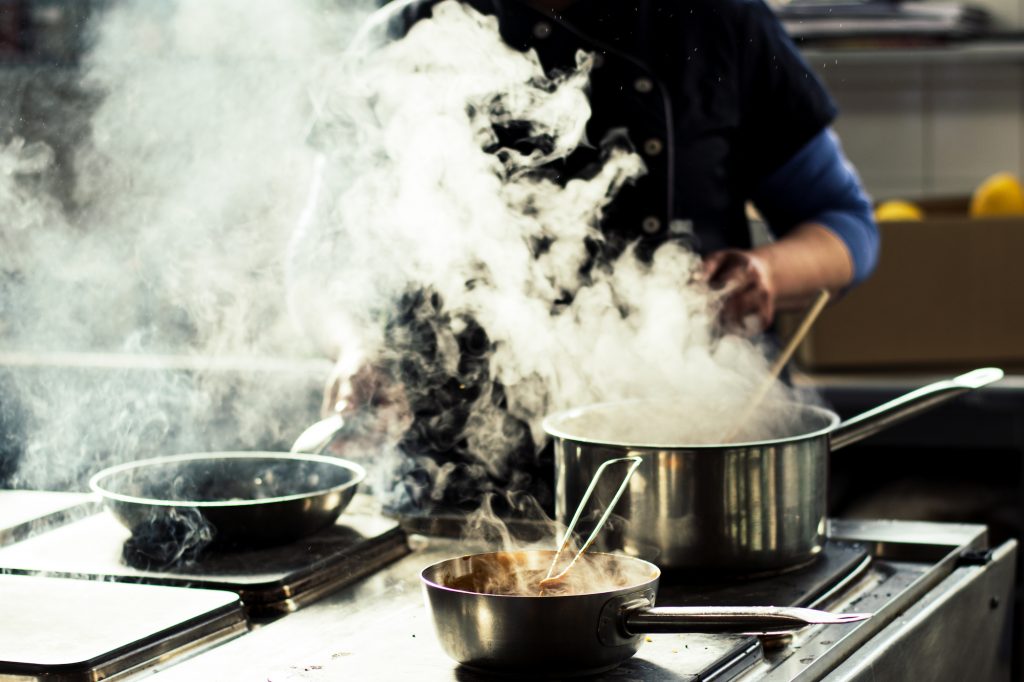 Chef cooking soup and water evaporating from a pot at a restaurant kitchen